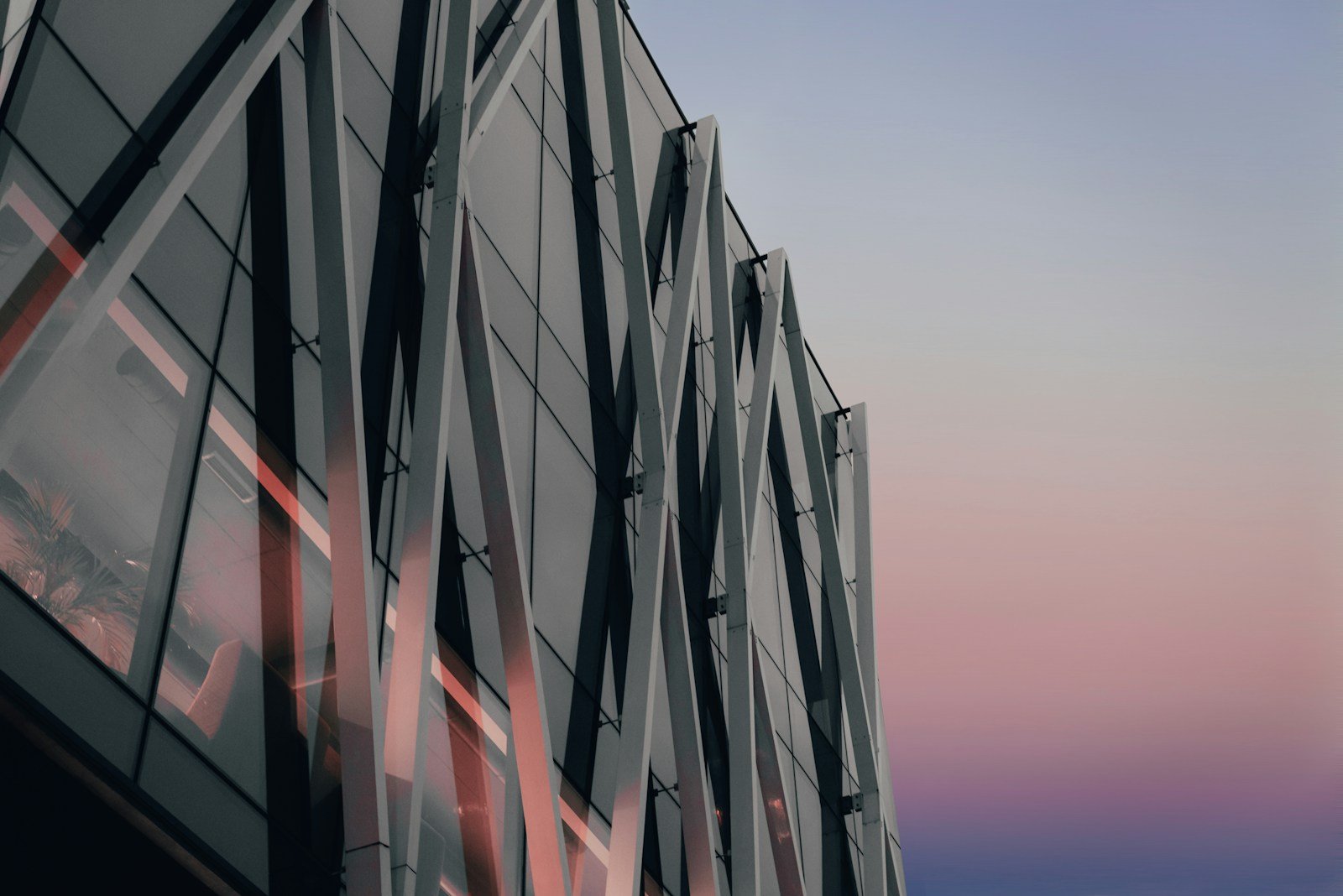 A glass building facade at twilight with layered reflections creating abstract geometric patterns, cool blue tones with fading amber light.