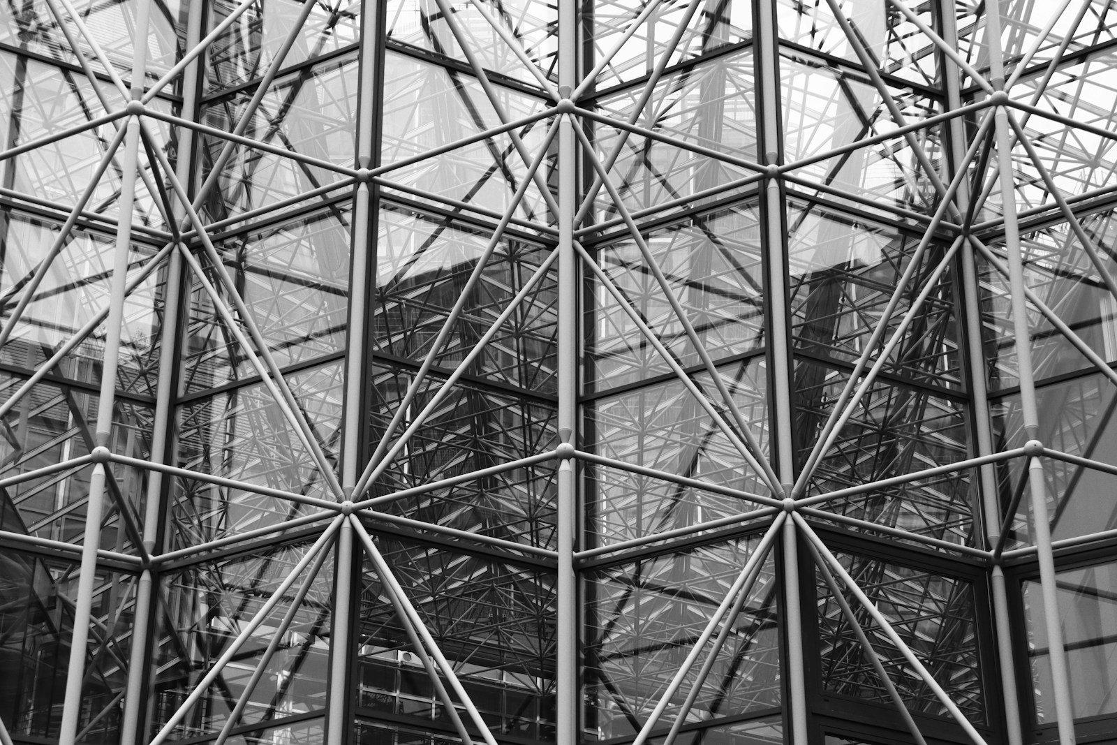 An abstract close-up of steel and glass structural framework forming a geometric grid pattern, rendered in black and white with cold industrial tones.