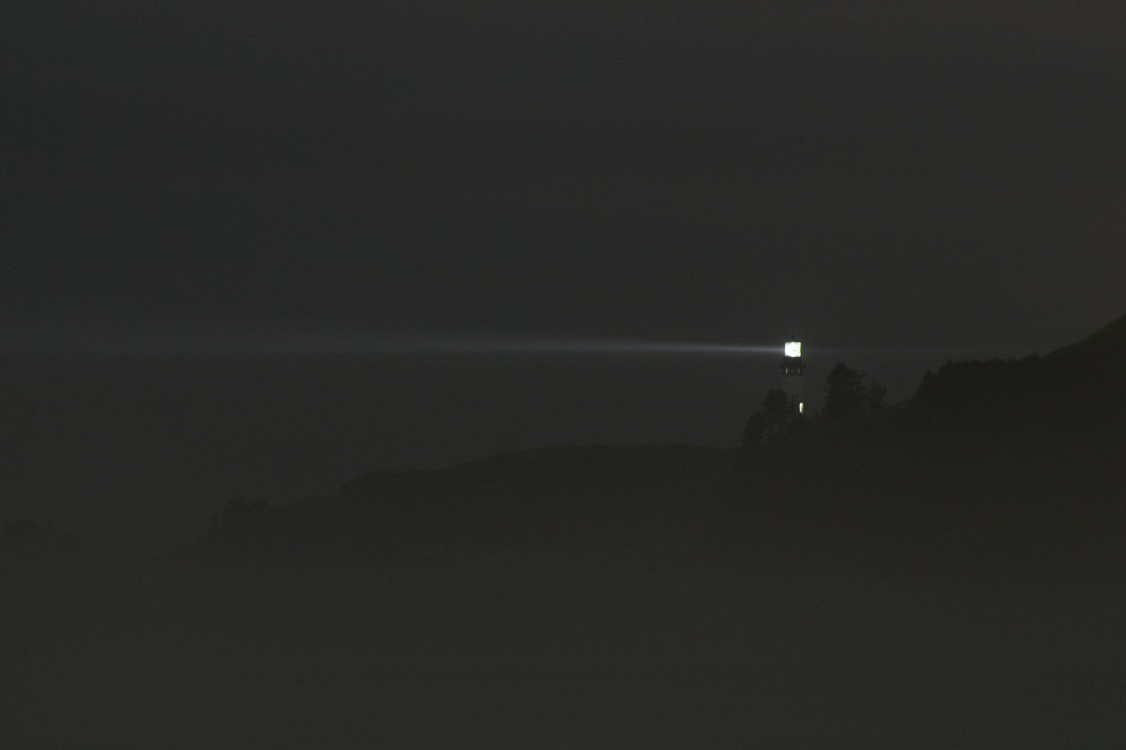 A single faint amber light glowing in dense fog at dusk, isolated against a dark background with no other visible features.