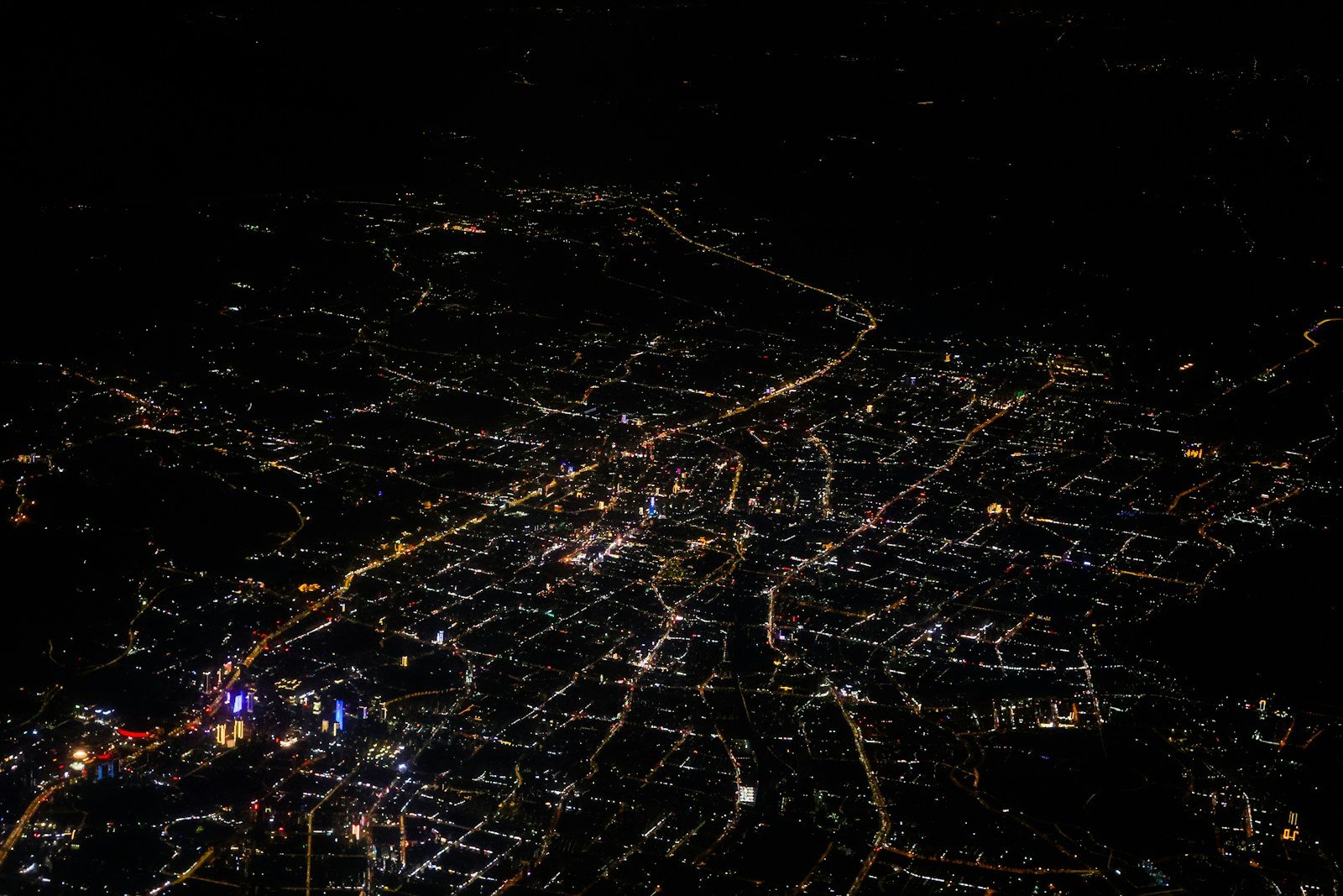 An aerial view of a city grid at night with scattered amber lights against a dark urban landscape, most buildings dark and unlit.