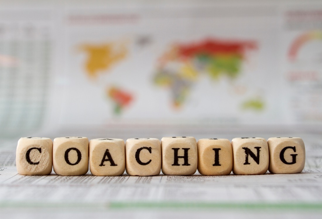 Wooden blocks spelling the word coaching with a blurred world map in the background.