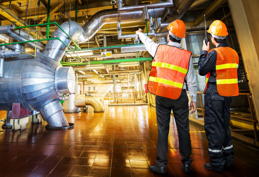 Two industrial improvement technicians in safety gear inspecting a manufacturing facility, highlighting process optimisation and efficiency improvements in industrial operations.