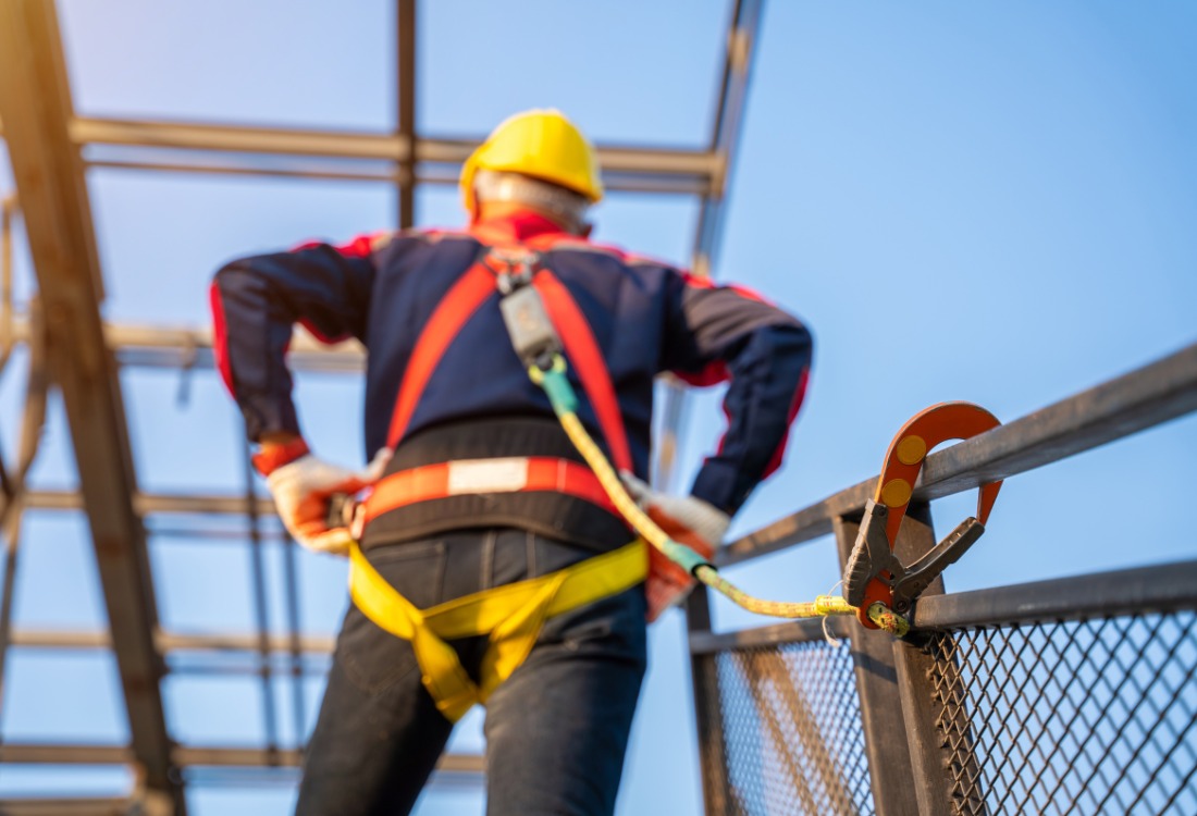 A construction worker wearing fall protection equipment and a safety harness secured to a railing, highlighting the importance of PASMA training in preventing workplace accidents and reducing costs.