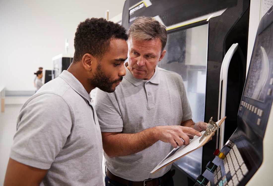 A senior trainer mentoring an apprentice in a manufacturing setting, highlighting the importance of employer investment in apprenticeship training and workforce development under the Apprenticeship Levy scheme.