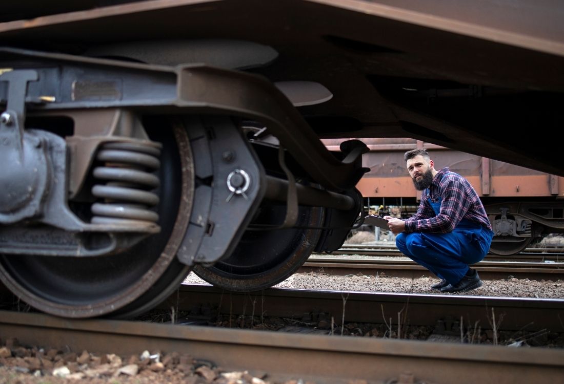 Rail engineering technician inspecting the undercarriage of a train carriage, representing the practical, hands-on nature of technician roles and essential maintenance training in the rail sector.