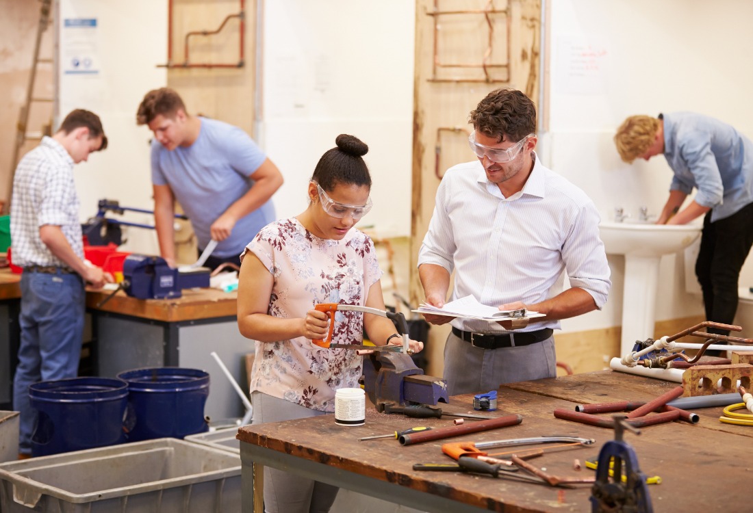 A group of apprentices working collaboratively in a wood workshop, guided by a professor in safety gear as they elevate industry skills through specialised training.
