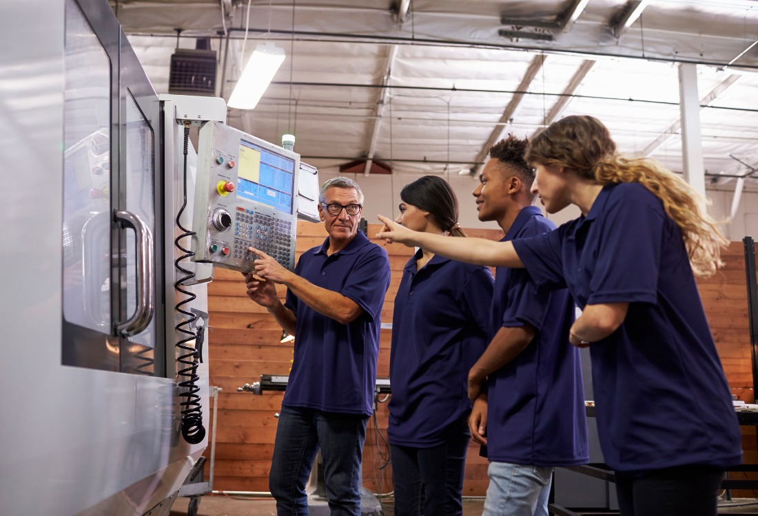 Engineering apprentices receiving hands-on training from an instructor on industrial machinery, illustrating the value of practical experience and mentorship in top-tier engineering apprenticeships.