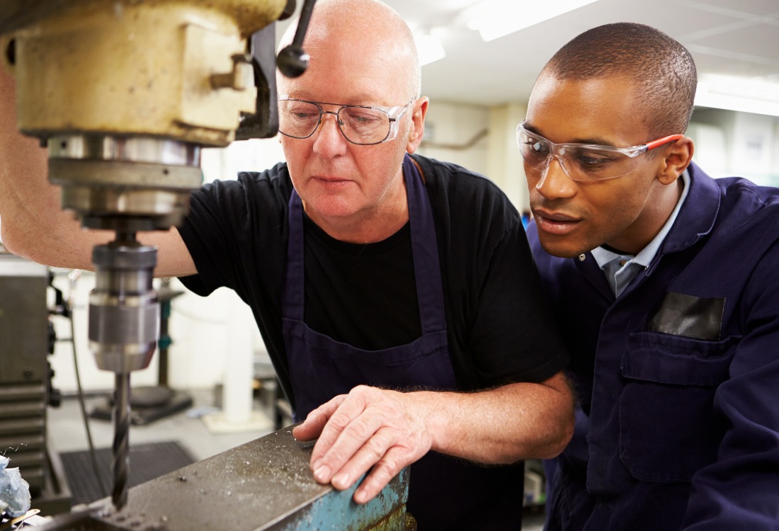 Experienced engineer mentoring a younger colleague on precision machinery, emphasising the role of continuous professional development in maintaining and enhancing engineering skills throughout a career.