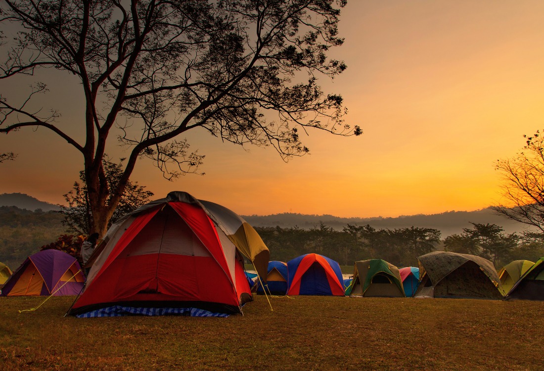Tents pitched on a hillside, facing a vibrant sunset sky.