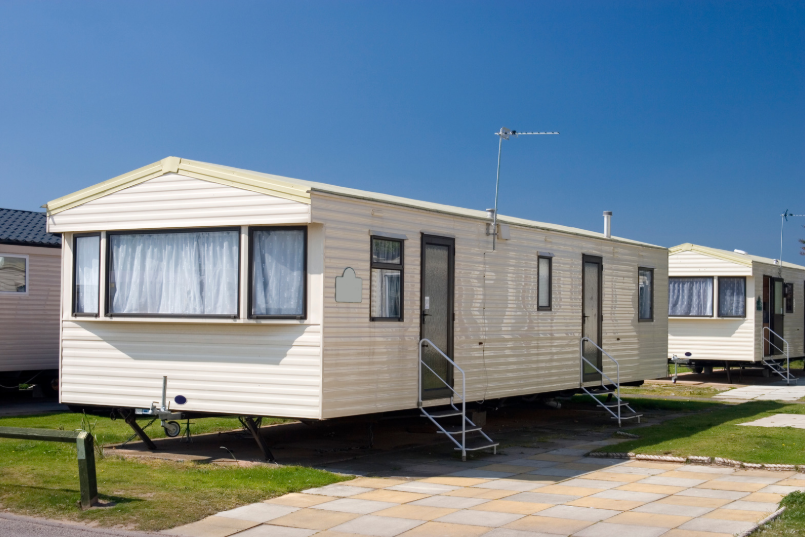A white static caravan on green grass with static caravan pods inside.