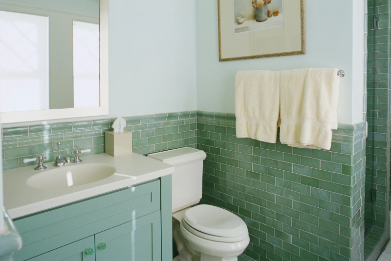 A bathroom with green tiles, a green bathroom cabinet and a toilet.