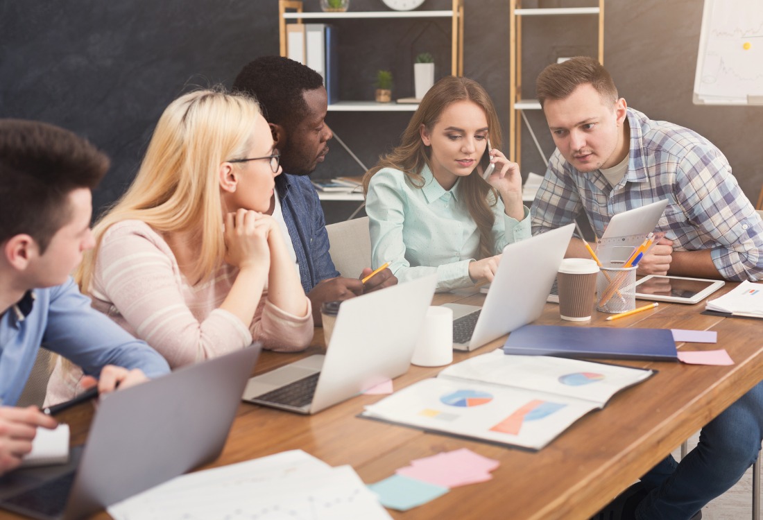Team of small business professionals collaborating at a desk with laptops and job tracking software charts.