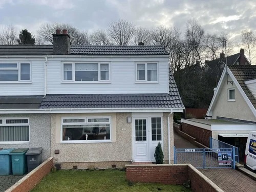Front view of a semi-detached Scottish home with a freshly coated roof under a cloudy sky.