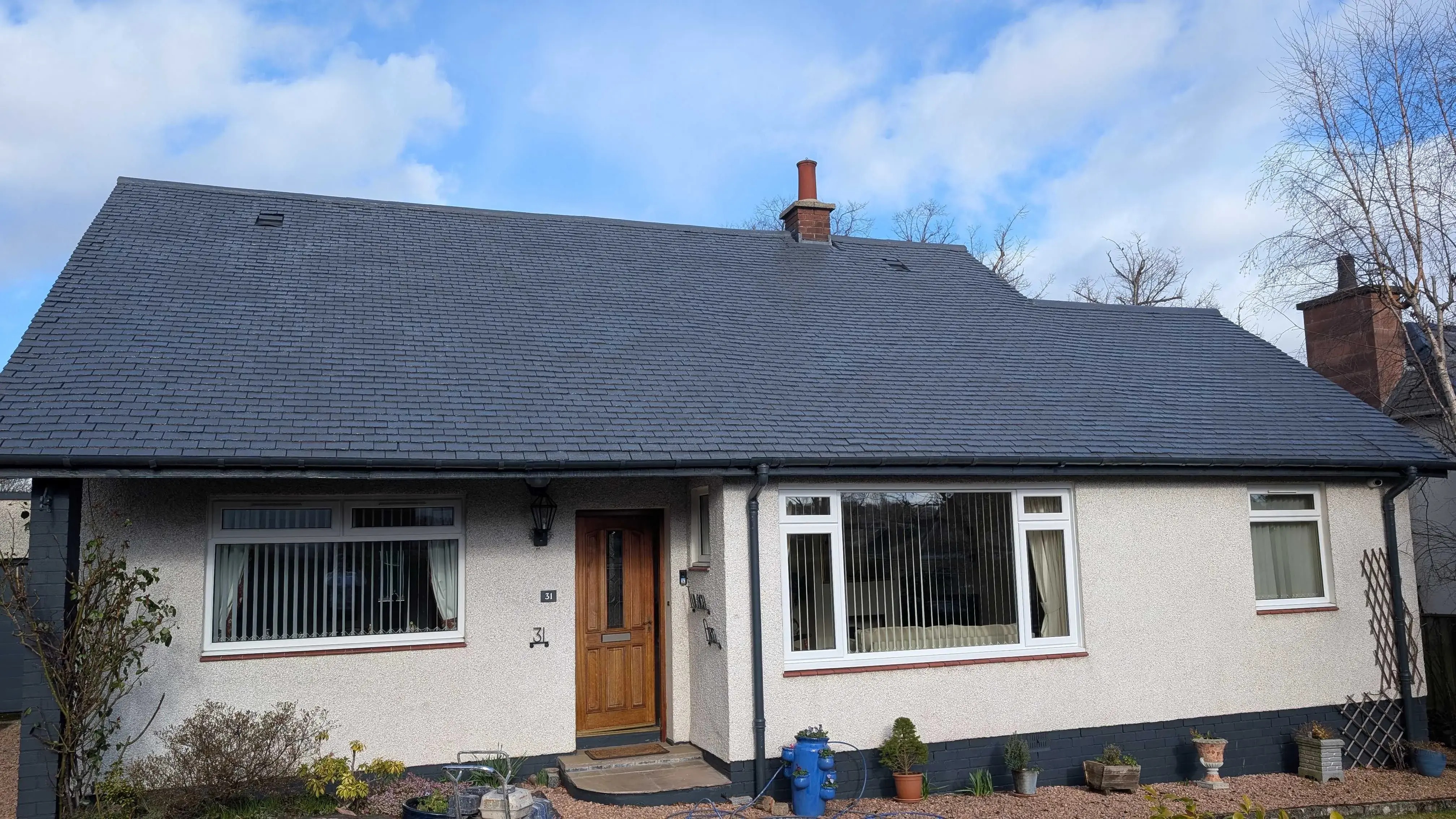 Single-storey Scottish home with a newly coated dark roof under a bright, partly cloudy sky.