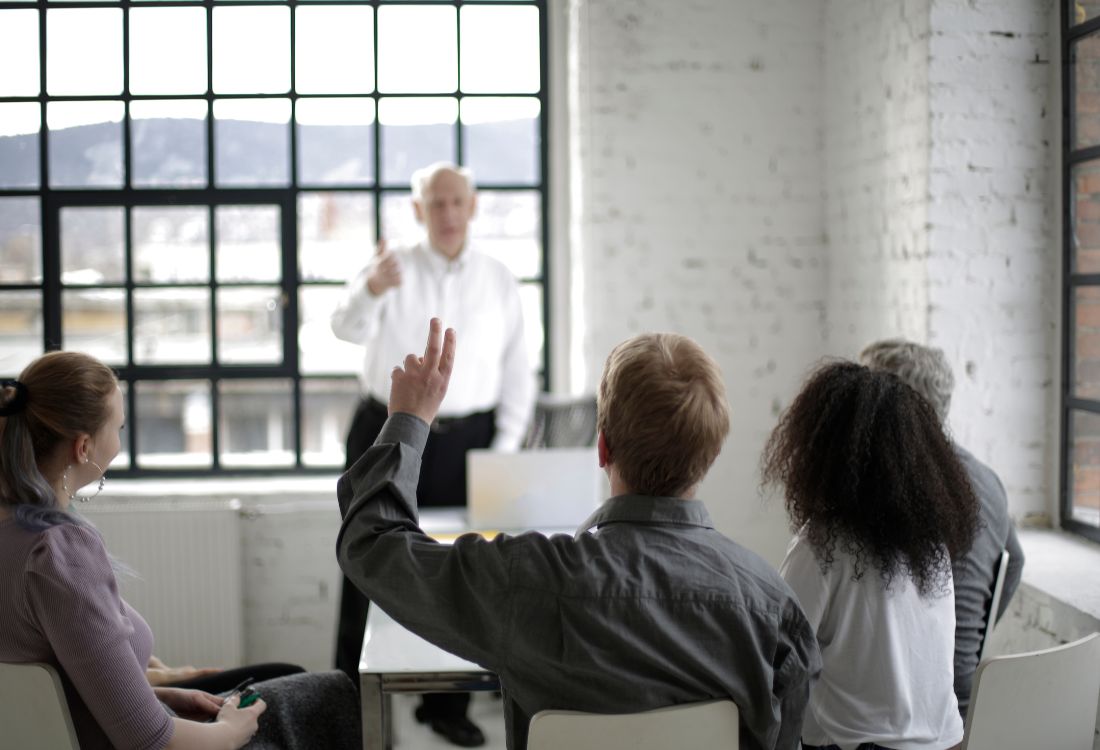 Business leader presenting to a small group during a meeting, with attendees raising hands in a modern office.