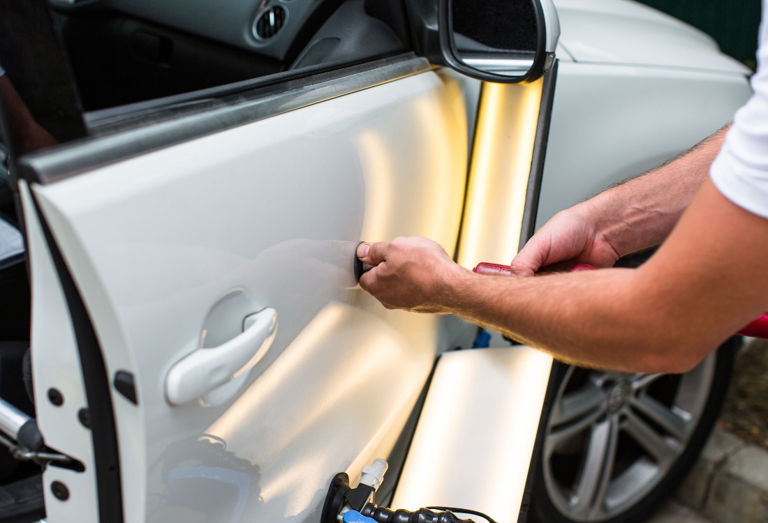 Mechanic repairing a dent on a car door during accident repair.