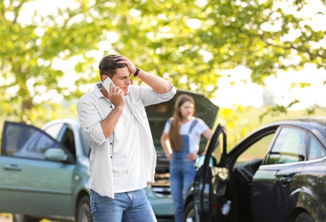 Car owner standing next to damaged vehicle with a hand on his head, representing the stress of accidents and the need for a courtesy car.