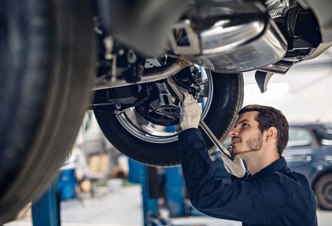 Certified mechanic working underneath a car at a Tesla-accredited repair centre to protect vehicle value and warranty.