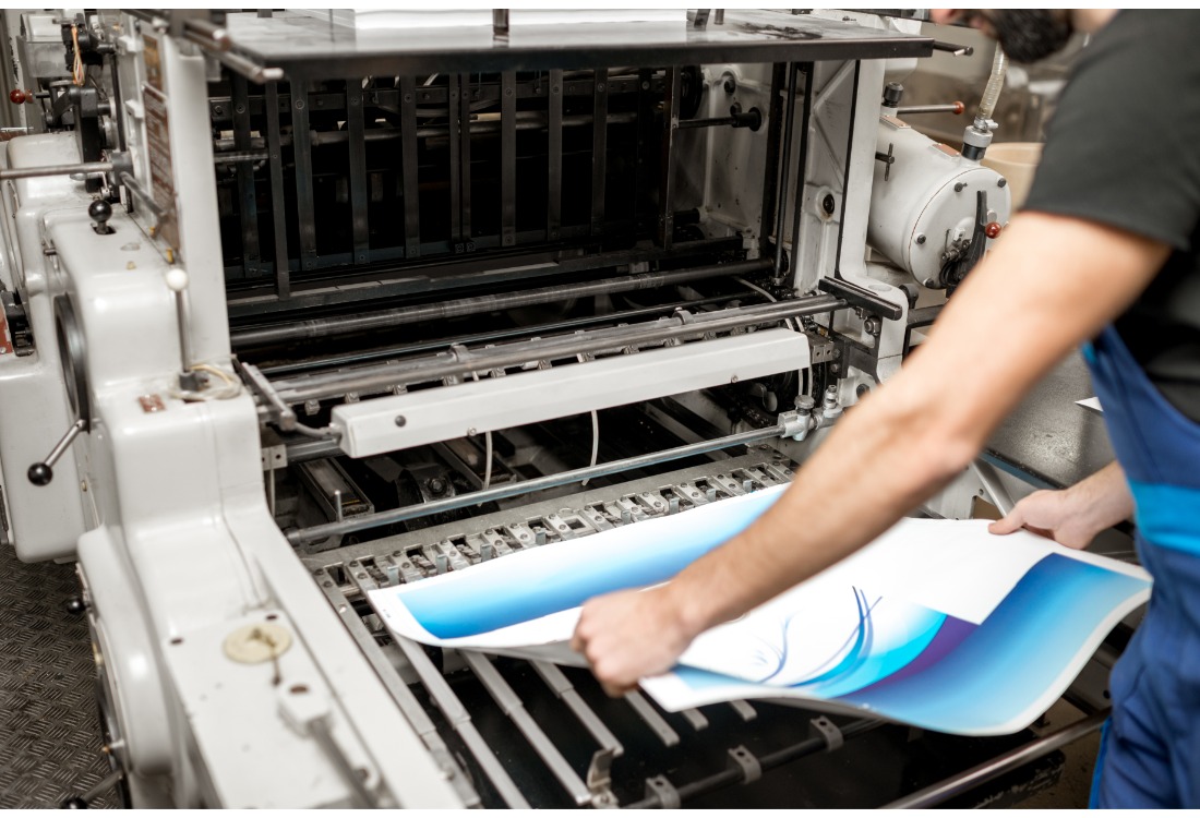 Print technician aligning freshly printed sheets on a commercial label printing press to ensure accurate production quality