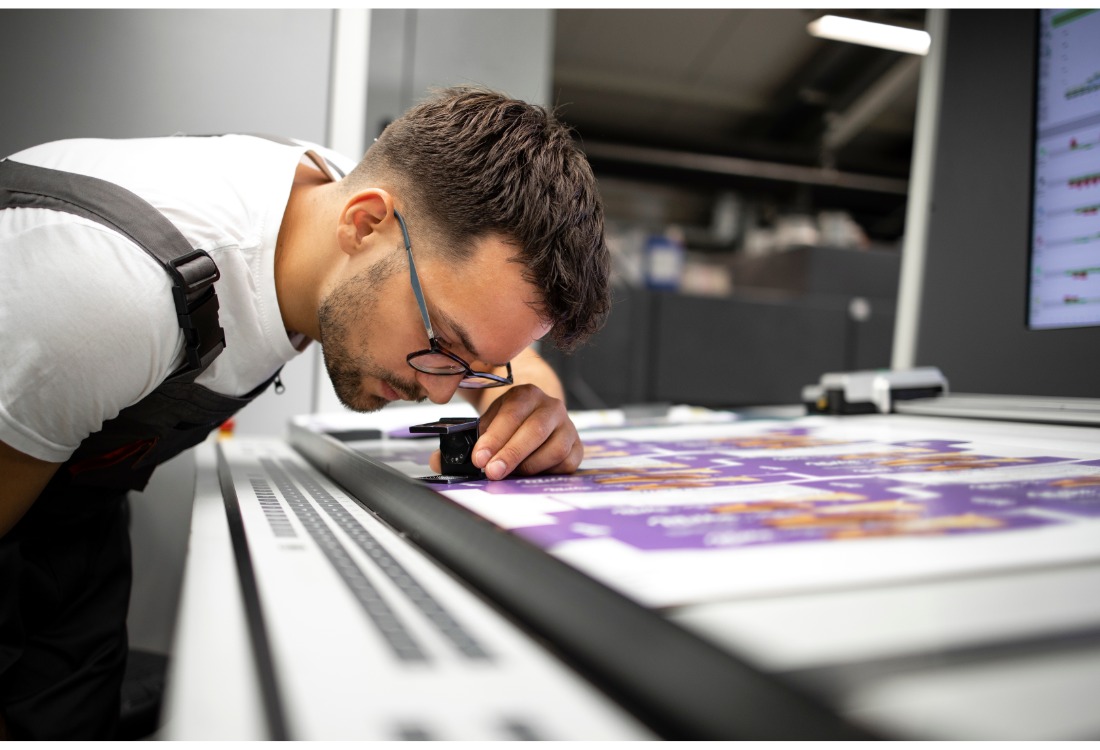 Print technician checking colour accuracy and quality on a freshly printed sheet in a professional label printing facility.