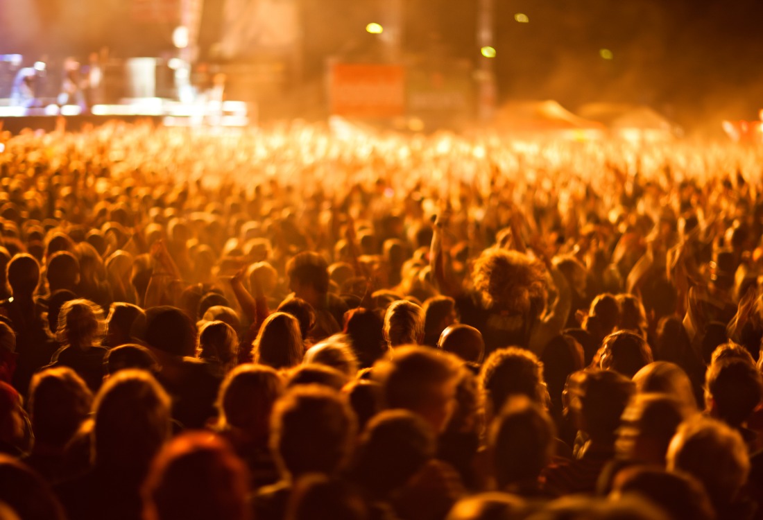 A large, excited crowd at a music venue, bathed in warm orange light. Temporary floor graphics being used for music venue crowd control, guiding the flow of attendees.