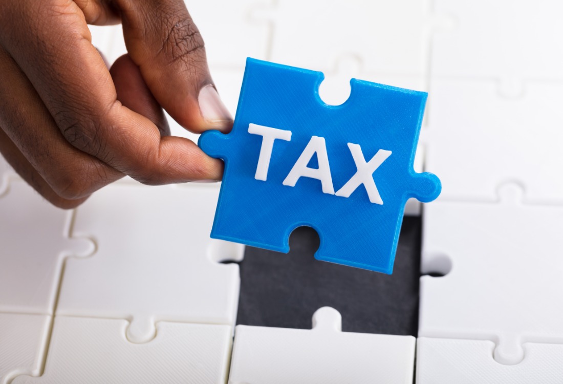 Hand holding a jigsaw puzzle piece with the word 'tax' on it. 