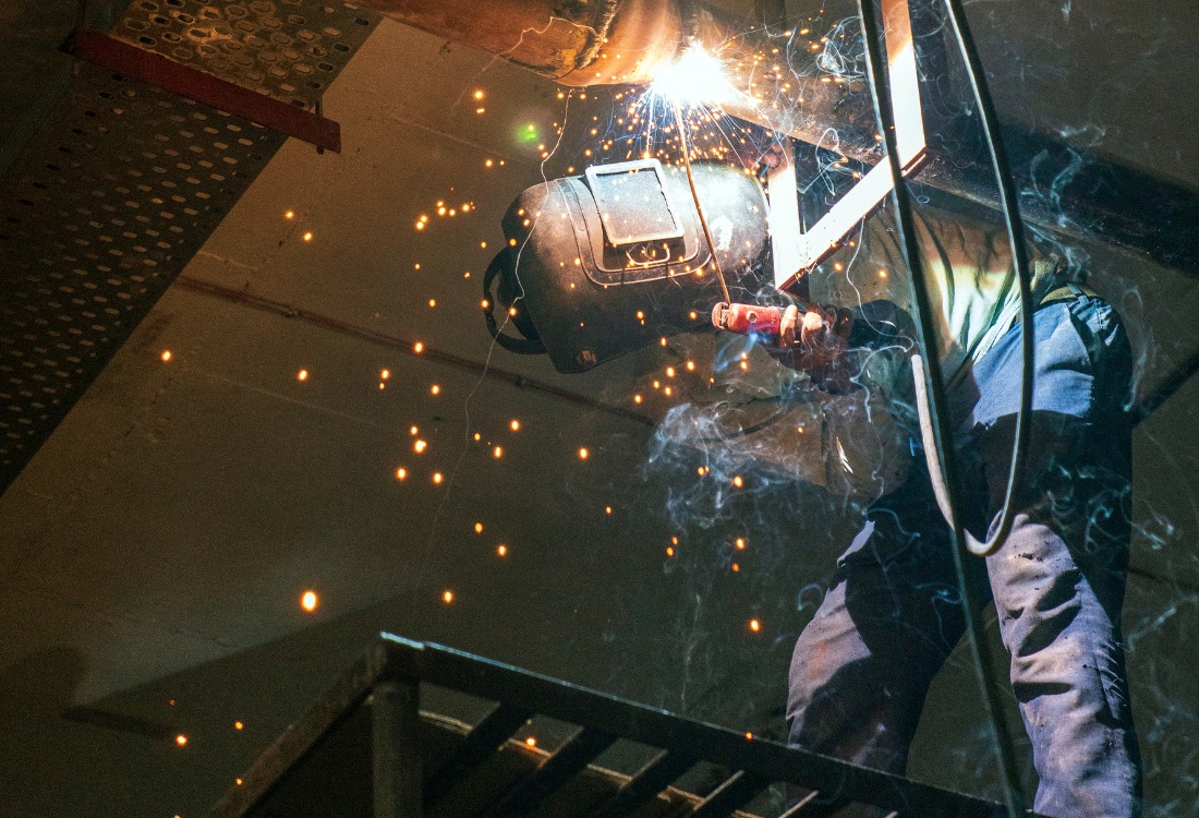 Industrial worker welding metal with sparks flying, highlighting workplace safety risks and vibration exposure control. 