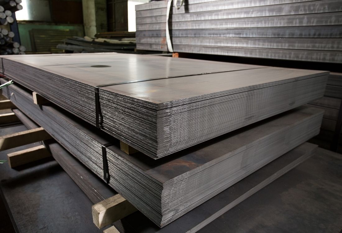 Close-up of stacks of precision-cut metal plates in an industrial warehouse, illustrating the importance of surface finishing standards in manufacturing for aerospace, automotive, and medical sectors. 