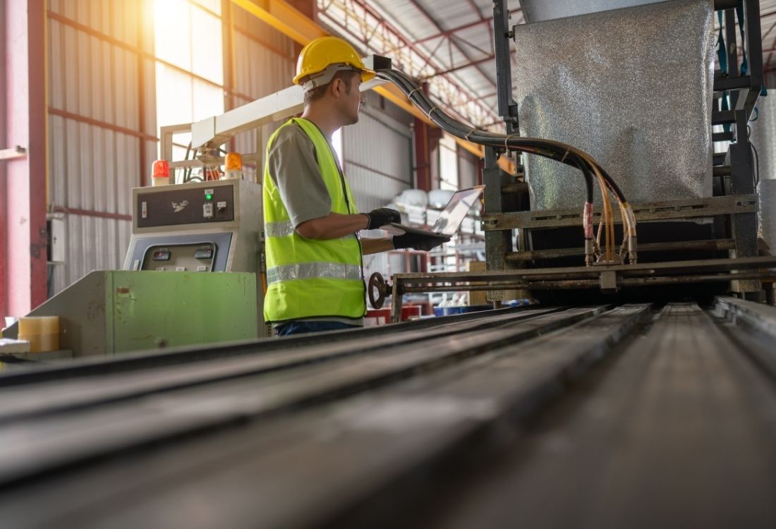 An engineer in safety gear inspecting the edge finishing of products on an automated machine line, highlighting the importance of quality control in UK manufacturing. 