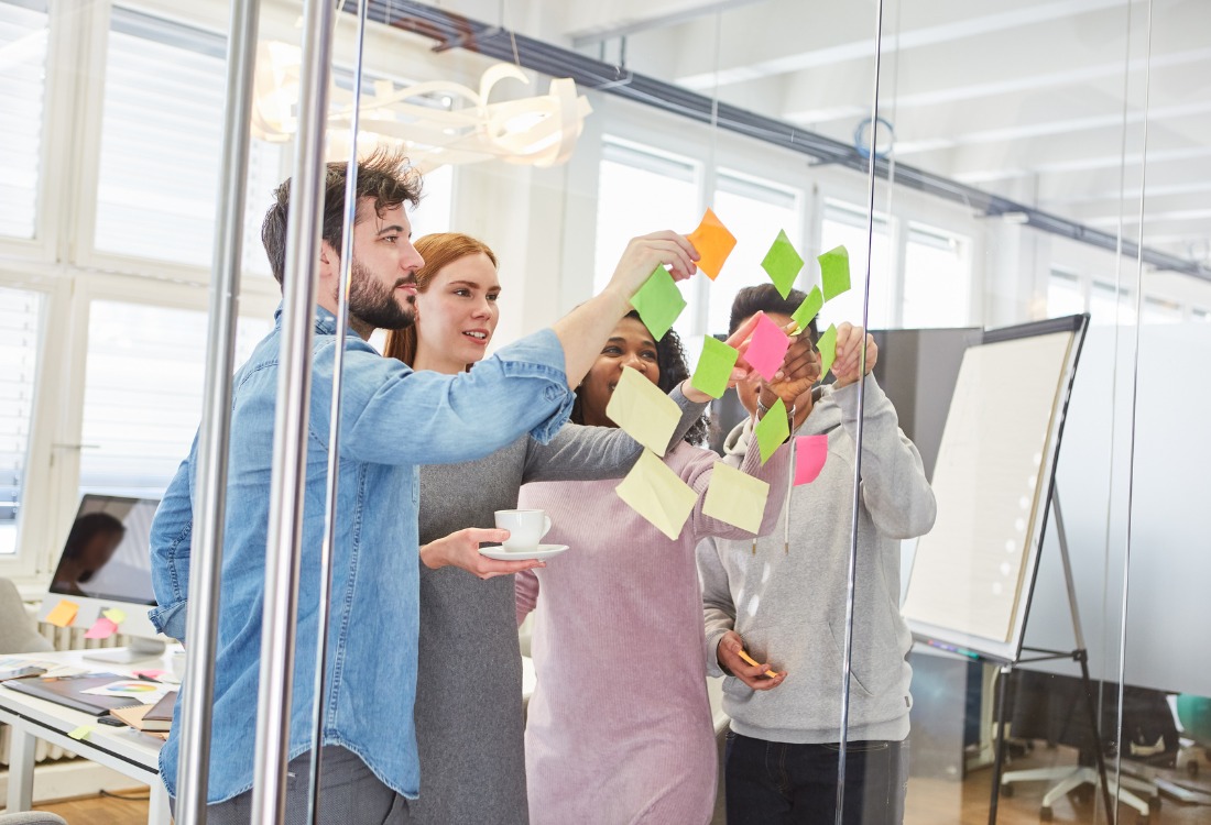 Team placing colourful sticky notes on a glass wall during a know yourself workshop.