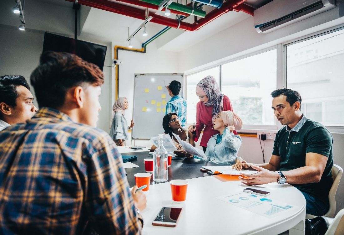 Colleagues gathered around a conference table, brainstorming with sticky notes on a whiteboard, illustrating teamwork during a learning and development programme session.