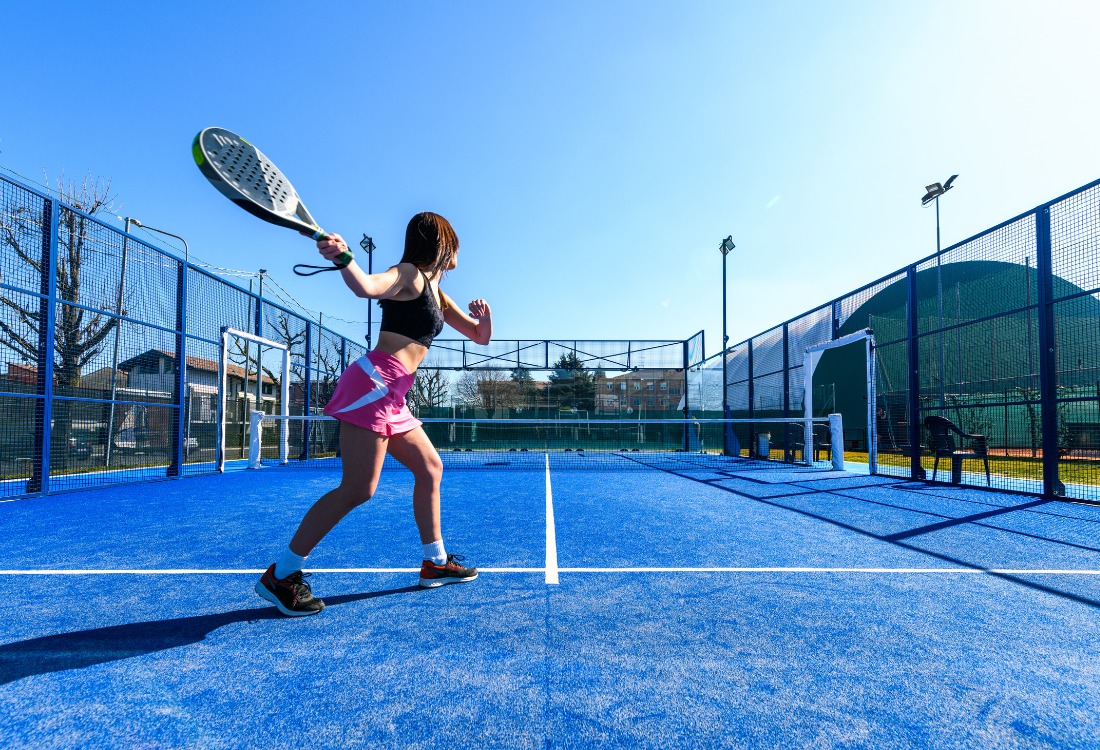 Young woman playing padel by herself on a modern blue outdoor court.