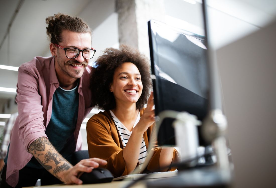 Two SME employees smiling and working together at a desktop computer, reflecting improved productivity and support from managed IT services in a modern office setting.