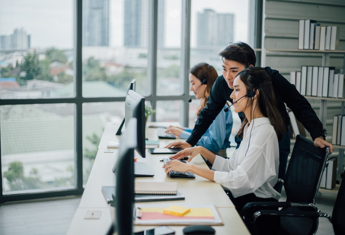 Call centre employees working at computers with headsets, supported by a colleague, showing how assistive technology and workplace tools can help employees with ADHD stay focused, manage tasks, and receive real-time guidance.