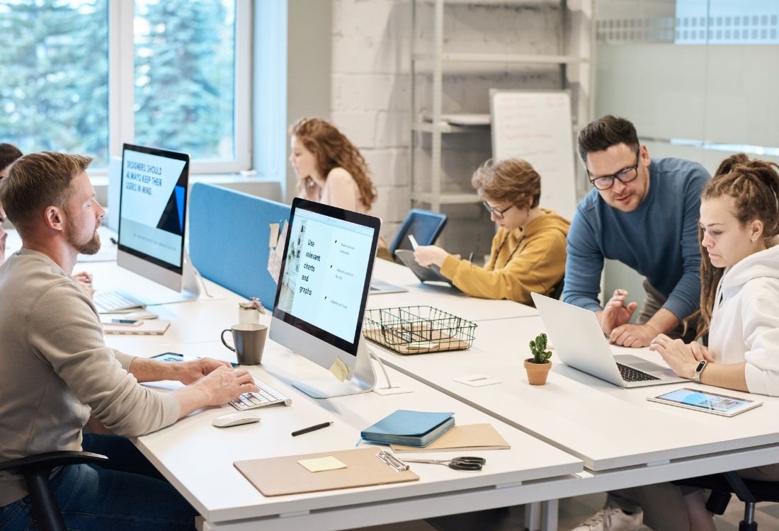 Modern office team working collaboratively across multiple devices, highlighting the contrast between internal IT processes and outsourced managed IT support in a dynamic business environment.