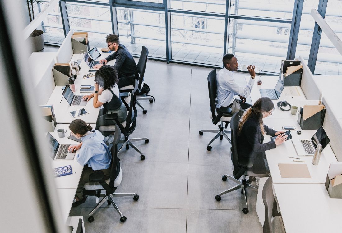 Office workers seated at individual desks in an open-plan workspace, illustrating the importance of ergonomic setups and shared responsibility for workplace wellbeing.