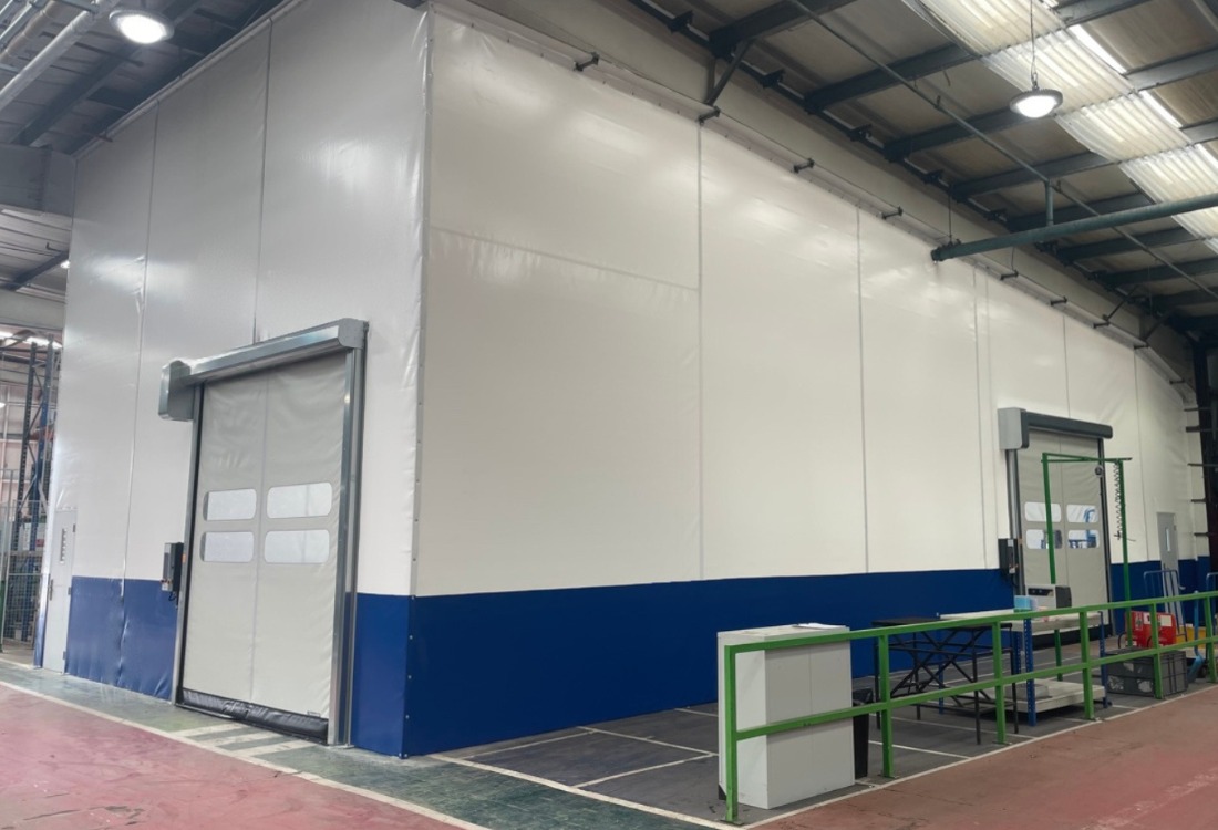White and blue food-grade flexible partition walls with high-speed doors in warehouse facility, creating controlled hygiene zone for allergen separation and food safety compliance.