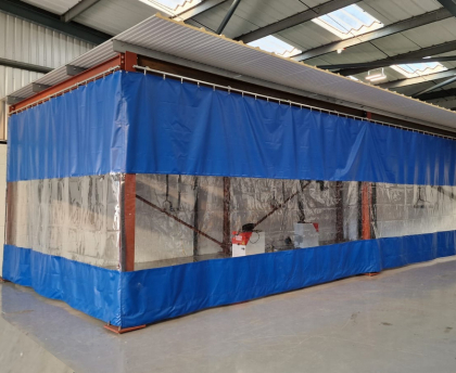 Blog cover image showing how industrial partition curtains prevent dust contamination, featuring a blue curtain with a clear viewing panel that isolates a work area from the rest of the facility.