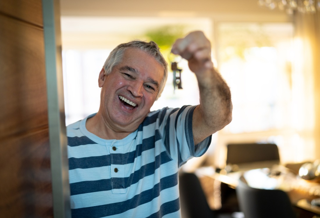 A picture of a man standing inside his non-standard house with his keys in his hands, smiling.