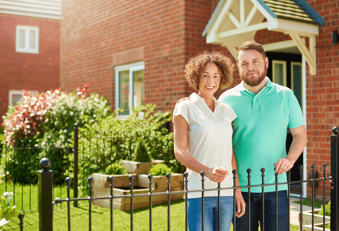 A couple standing in front of a non-standard house on a sunny day.