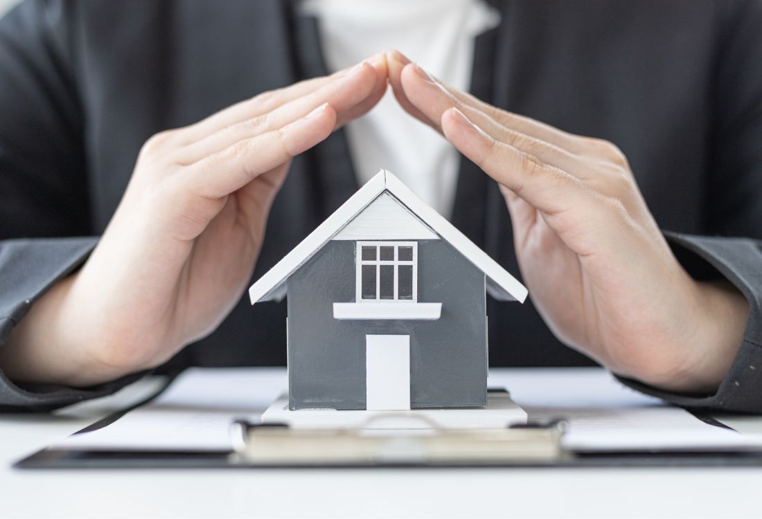 Hands protecting a model house representing home insurance subsidence cover.