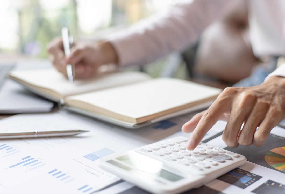 Close-up of a person working with a calculator, financial spreadsheets, and a notebook.