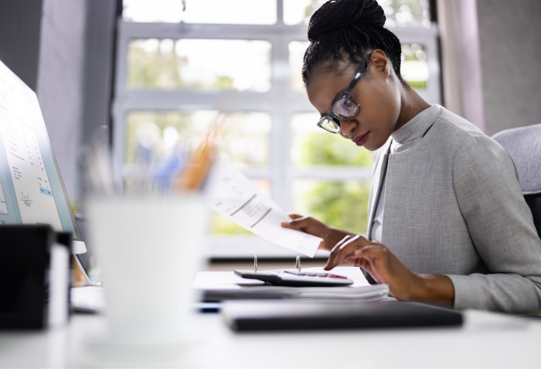 Management accountant reviewing financial documents and calculating figures at a desk in a modern office.