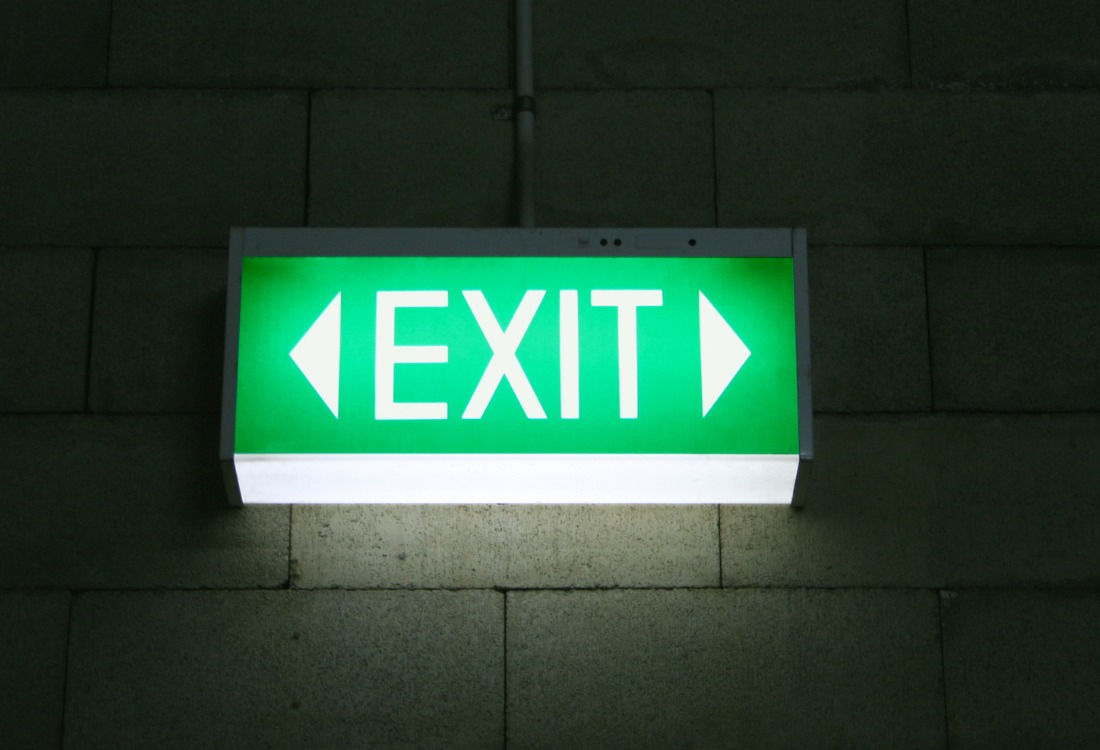 Green emergency exit sign illuminated for building safety compliance and testing standards.
