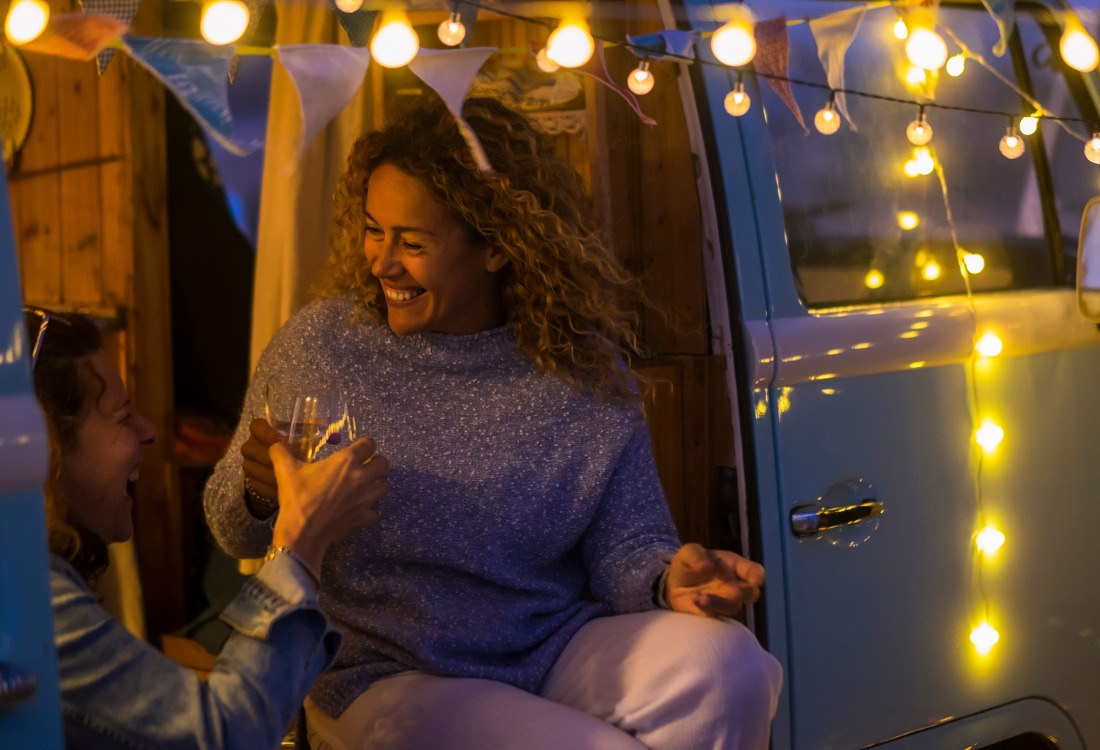 Friends raising drinks inside a festive campervan parked by a Christmas market, illustrating a joyful campervan trip during the holiday season.