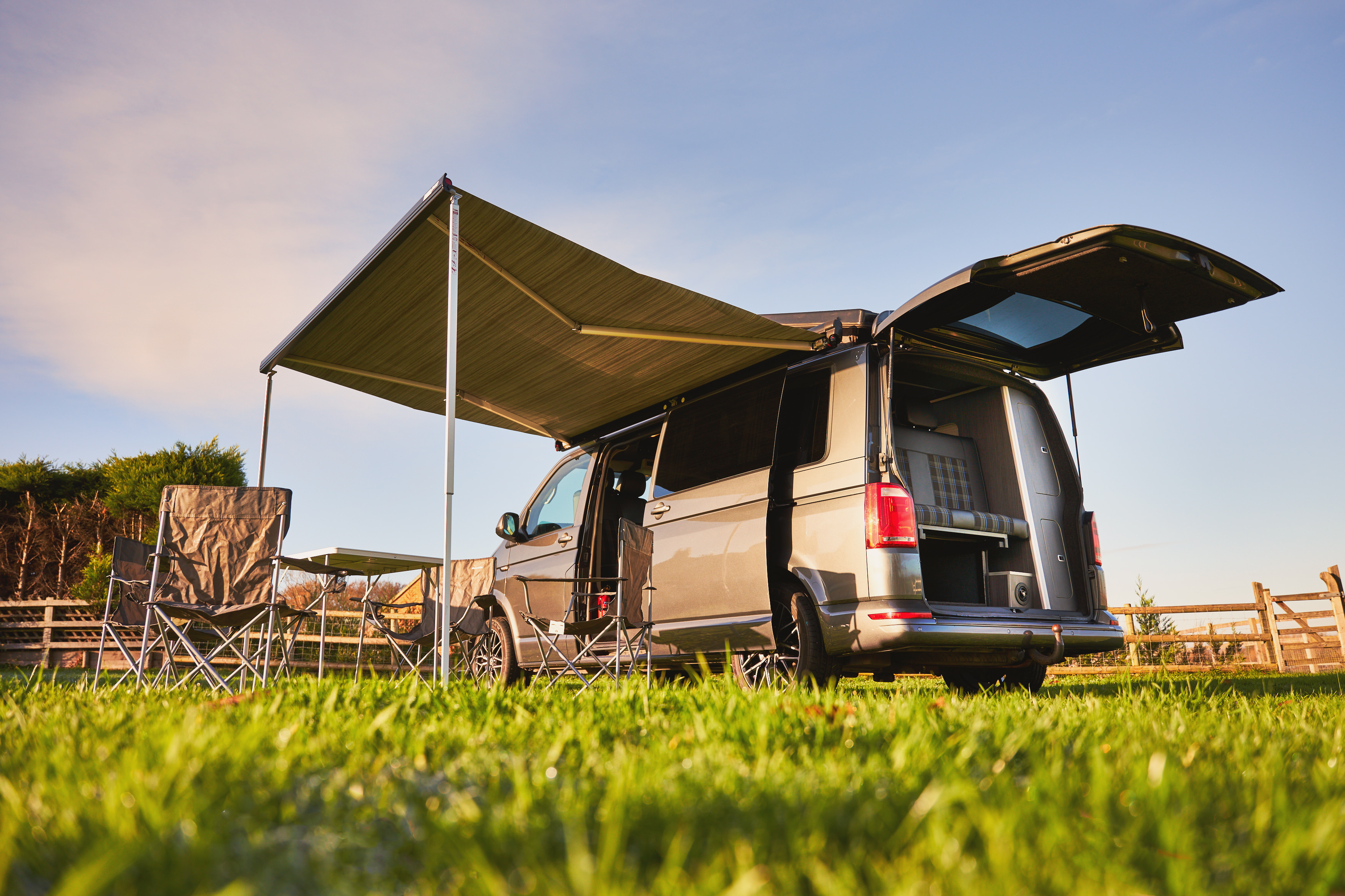 Campervan equipped with solar panels on the roof, parked with awning and camping chairs, highlighting the durability and lifespan of solar panels for campervan roofs.