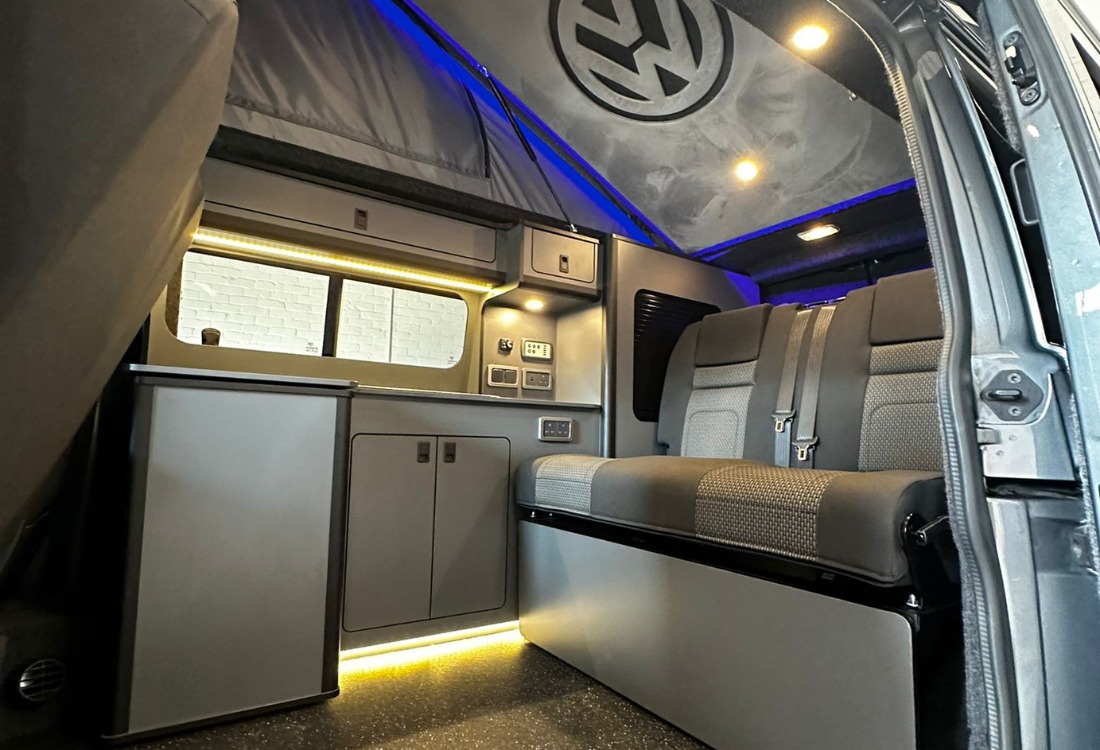 Interior view of a campervan upgrade featuring fitted kitchen units, seating, and compact design for travel.