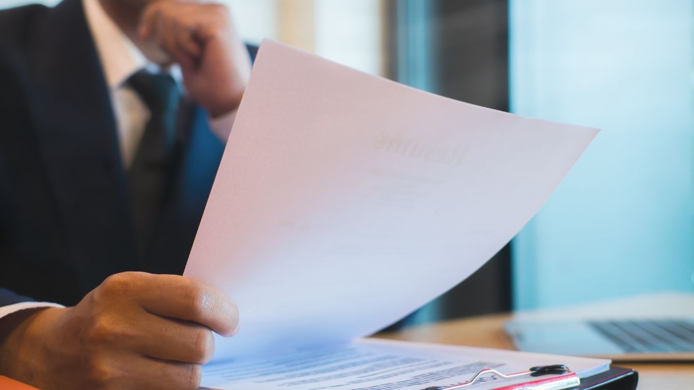 An evaluator holding a document while Reading QC Reports with a laptop in the background.
